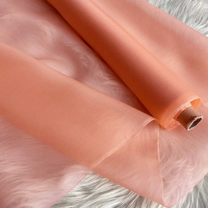 A partially unrolled piece of Longan Craft Multicolor 8 Momme Organza Silk Fabric By The Yard—pure mulberry silk—rests on a white surface, showcasing its soft, lightweight, and slightly translucent qualities ideal for dresses.