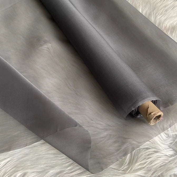 A roll of Longan Craft Multicolor 8 Momme Organza Silk Fabric By The Yard, made from pure mulberry silk, is partially unrolled on a soft white surface. This lightweight, translucent luxury silk is ideal for crafting elegant dresses.