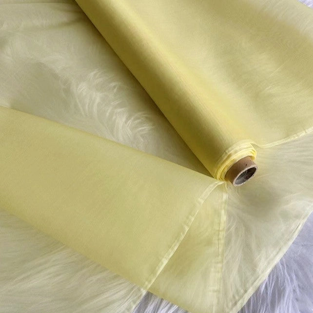 A roll of Longan Craft Multicolor 8 Momme Organza Silk Fabric By The Yard, pure mulberry silk, partially unrolled on a white surface. This translucent, airy luxury fabric is perfect for crafting elegant dresses and evening gowns.