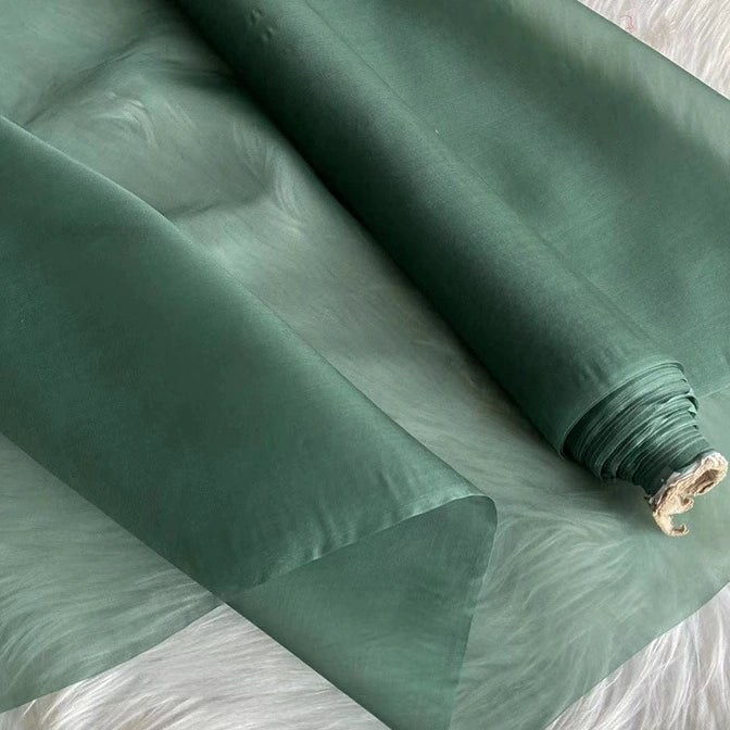 A roll of Longan Craft Multicolor 8 Momme Organza Silk Fabric By The Yard, made from pure mulberry silk, is partially unrolled to reveal its smooth and translucent finish—ideal luxury material for elegant dresses.