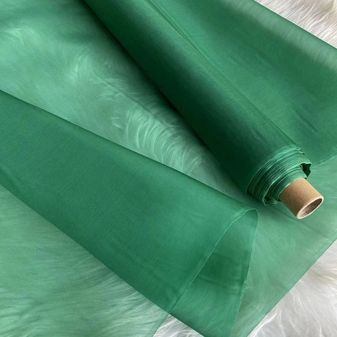 A roll of Longan Craft Multicolor 8 Momme Organza Silk Fabric by the yard, made from pure Mulberry silk, is partially unrolled on a white surface—showcasing its smooth, translucent texture for luxurious dresses and gowns.