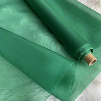A roll of Longan Craft Multicolor 8 Momme Organza Silk Fabric by the yard, made from pure Mulberry silk, is partially unrolled on a white surface—showcasing its smooth, translucent texture for luxurious dresses and gowns.