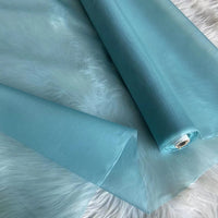 A roll of Longan Craft's Multicolor 8 Momme Organza Silk Fabric By The Yard, made from pure mulberry silk, is partly unrolled on a white furry surface. Its delicate, semi-transparent luxury is ideal for elegant dresses and evening gowns.