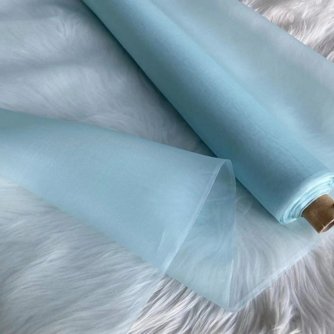 A roll of Longan Craft Multicolor 8 Momme Organza Silk Fabric By The Yard, made of pure Mulberry silk, is partially unrolled on a white surface, showcasing its luxurious and delicate texture—ideal for elegant dresses.
