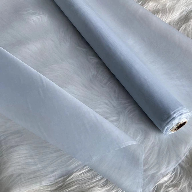 A roll of Multicolor 8 Momme Organza Silk Fabric by Longan Craft is unrolled on a white, fluffy surface. This pure mulberry silk material looks delicate and translucent—luxury fabric by the yard, ideal for elegant dresses.