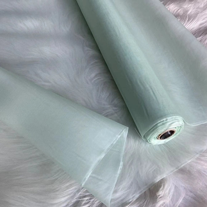 A roll of Multicolor 8 Momme Organza Silk Fabric by Longan Craft, made from pure mulberry silk, is displayed on a soft white surface. This lightweight, translucent luxury material is ideal for crafting elegant dresses.