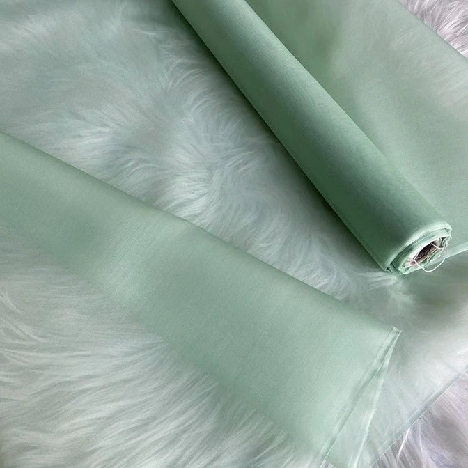 Two rolls of Multicolor 8 Momme Organza Silk Fabric By The Yard from Longan Craft are displayed on white faux fur, highlighting their soft, translucent texture—ideal luxury pure mulberry silk material for delicate dresses and evening gowns.