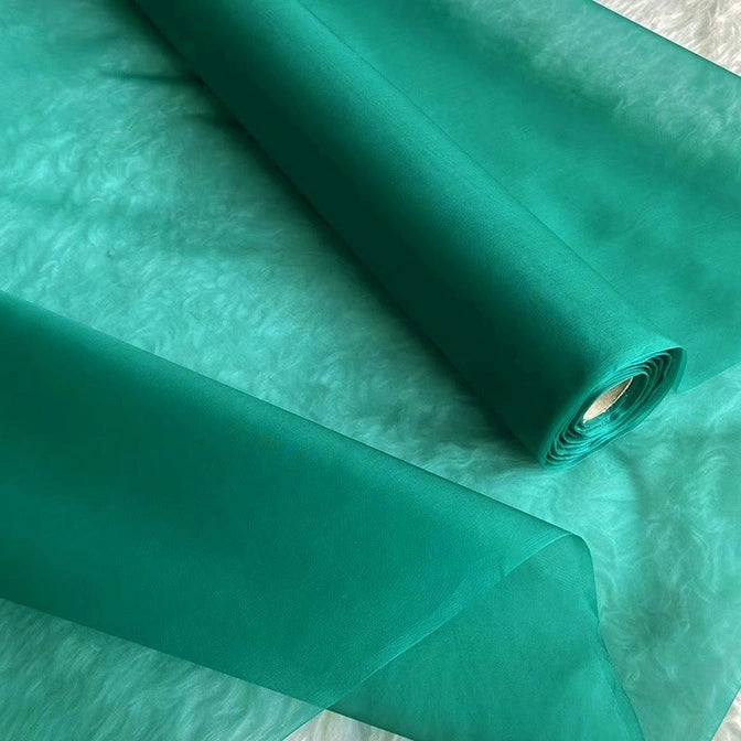 Two rolls of Longan Craft Multicolor 8 Momme Organza Silk Fabric by the yard are unrolled on a textured white surface. This pure mulberry silk is lightweight, slightly transparent, and ideal for luxury dresses or decorative accents.
