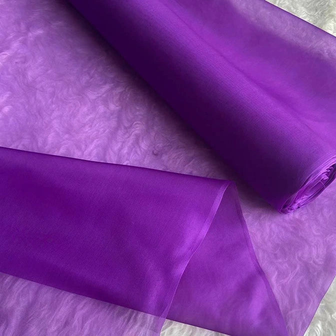 Two rolls of Longan Craft Multicolor 8 Momme Organza Silk Fabric by the yard, made from pure mulberry silk, are displayed on a textured surface—luxurious, glossy, and ideal for elegant evening gowns and dresses.