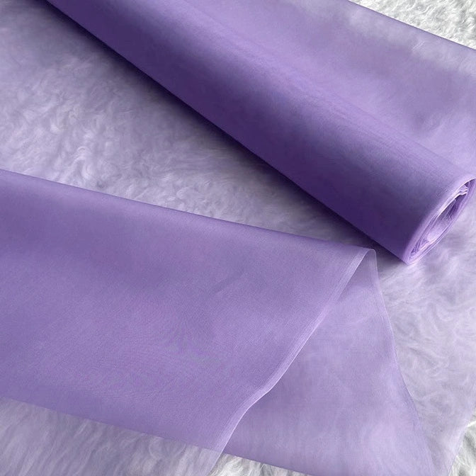 A roll of Multicolor 8 Momme Organza Silk Fabric by Longan Craft is displayed on a textured white surface, highlighting its delicate translucence—ideal for luxury dresses or pairing with other pure Mulberry silk fabrics for stunning creations.