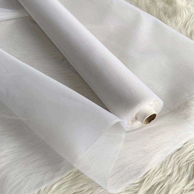A roll of Multicolor 8 Momme Organza Silk Fabric by Longan Craft is unrolled on a soft, white surface. This pure mulberry silk material appears delicate and translucent—ideal for creating luxury dresses and elegant gowns.