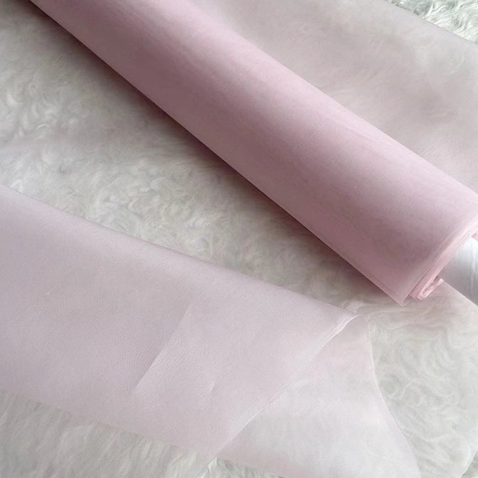 A roll of Longan Craft Multicolor 8 Momme Organza Silk Fabric by the yard, pure Mulberry silk ideal for luxury dresses, is displayed on a white textured surface, showcasing its soft, sheer, and delicate quality.