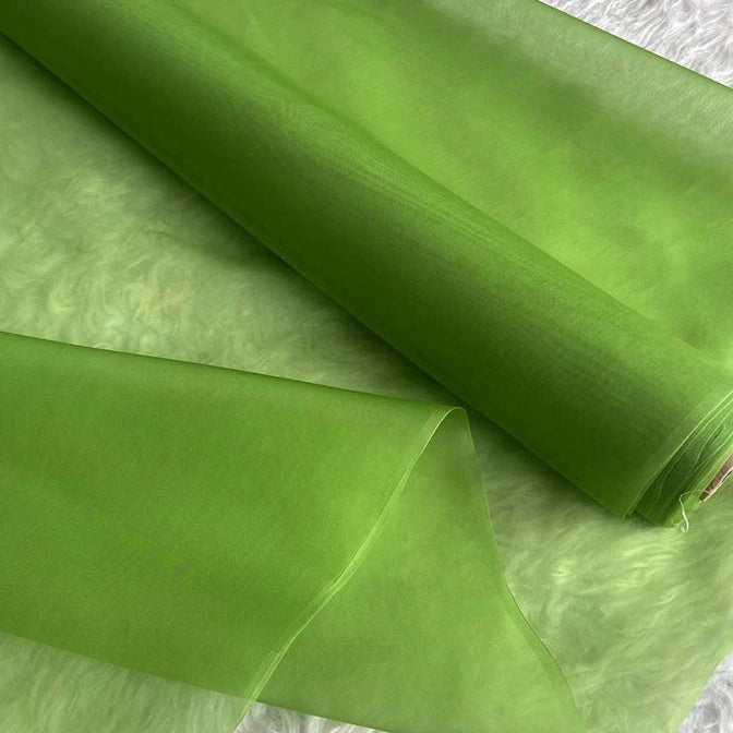 A roll of Longan Craft Multicolor 8 Momme Organza Silk Fabric By The Yard, made from pure mulberry silk, is partially unrolled on a light, textured surface. The luxury silk for dresses looks lightweight and slightly translucent.