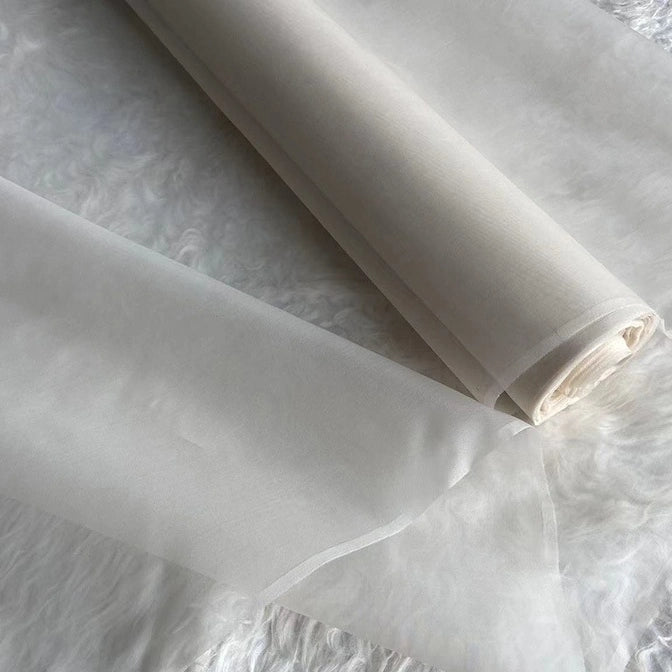 A roll of Longan Craft Multicolor 8 Momme Organza Silk Fabric By The Yard, made from pure mulberry silk, is partially unrolled on a soft white surface, showcasing its luxurious, delicate, and translucent texture ideal for dresses.