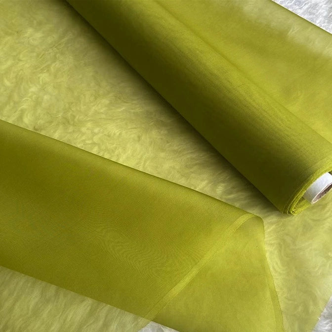 A close-up of two rolls of Longan Craft’s Multicolor 8 Momme Organza Silk Fabric by the yard, pure Mulberry silk material, showing the smooth, translucent, slightly shiny luxury fabric unrolled on a textured surface.