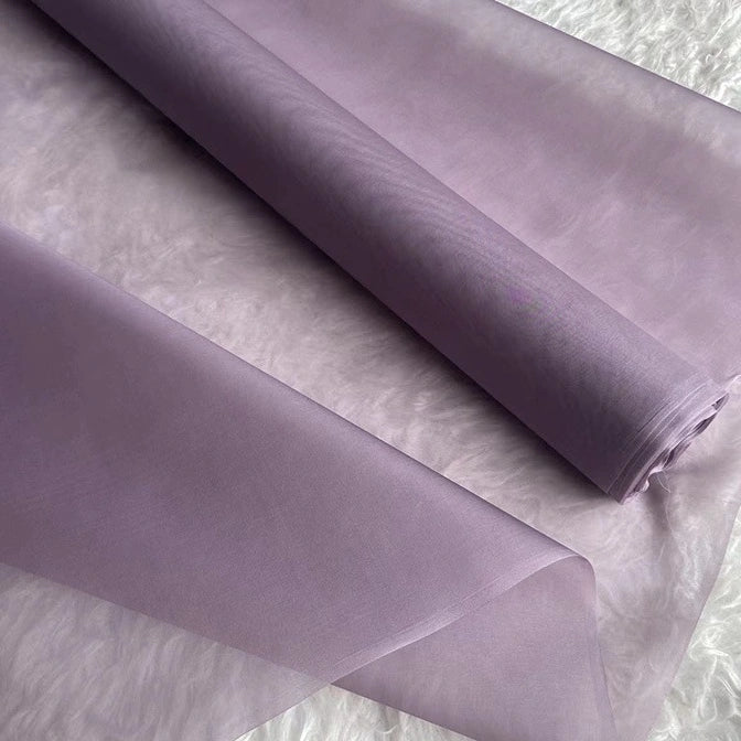 A close-up of Longan Craft’s Multicolor 8 Momme Organza Silk Fabric By The Yard, made from pure mulberry silk, partially unrolled on a textured white surface. Ideal luxury material for dresses.