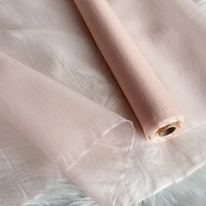 A roll of Multicolor 8 Momme Organza Silk Fabric by Longan Craft is unrolled on a white surface. This pure mulberry silk material is sheer, delicate, and airy—ideal luxury fabric for elegant evening dresses.