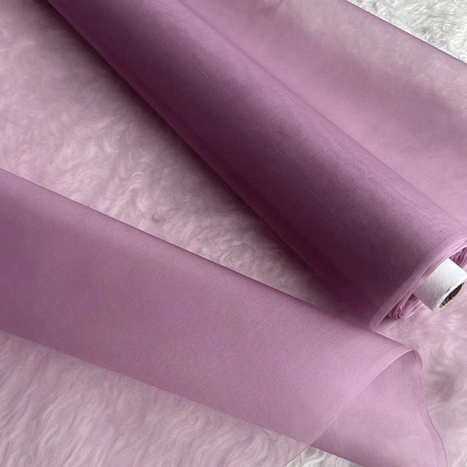 Two rolls of Multicolor 8 Momme Organza Silk Fabric by Longan Craft are unrolled on a white textured surface. This pure mulberry silk fabric is sheer, smooth, and delicate—luxurious material perfect for elegant dresses.