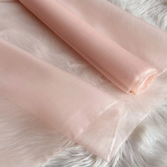 Two rolls of Longan Craft Multicolor 8 Momme Organza Silk Fabric are shown on a soft, white surface. This pure mulberry silk material is lightweight, slightly sheer, and perfect for creating luxury dresses.