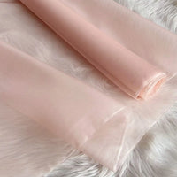 Two rolls of Longan Craft Multicolor 8 Momme Organza Silk Fabric are shown on a soft, white surface. This pure mulberry silk material is lightweight, slightly sheer, and perfect for creating luxury dresses.