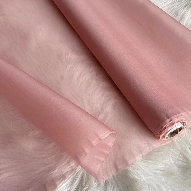 A roll of Longan Craft Multicolor 8 Momme Organza Silk Fabric By The Yard, made from pure mulberry silk, lies unrolled on a white furry surface—its smooth, translucent finish makes it ideal for luxury dresses and evening gowns.