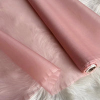 A roll of Longan Craft Multicolor 8 Momme Organza Silk Fabric By The Yard, made from pure mulberry silk, lies unrolled on a white furry surface—its smooth, translucent finish makes it ideal for luxury dresses and evening gowns.