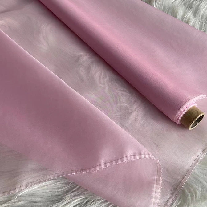 A close-up of Longan Craft’s Multicolor 8 Momme Organza Silk Fabric by the yard—pure mulberry silk—rests on a soft, white, furry surface. The delicate luxury fabric is perfect for dresses, with one sheer edge gently folded.