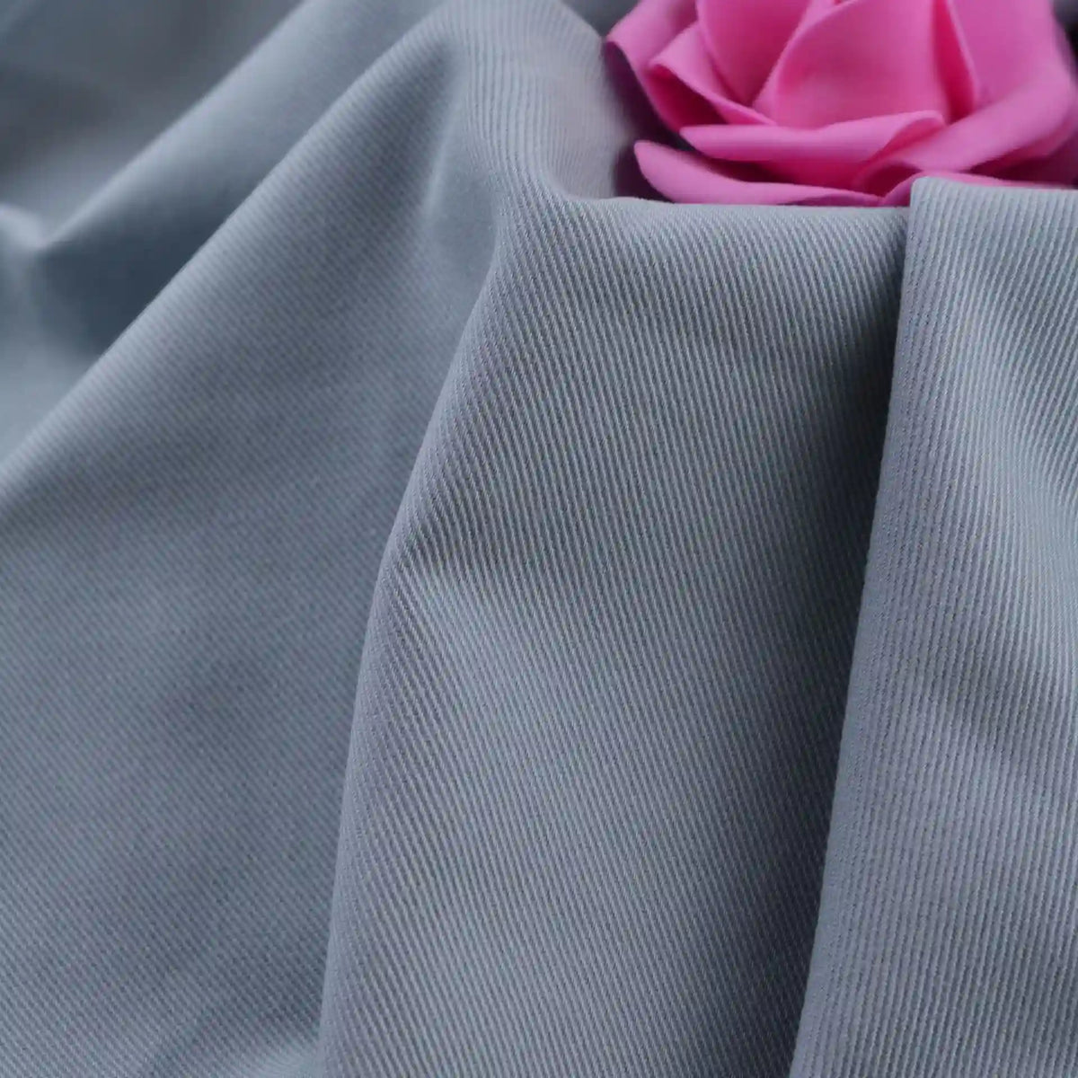 A close-up of Longan Craft’s Multicolor Cotton Bamboo Blend Lyocell Fabric by the yard, shown in light grey with ribbed texture and soft folds, features a pink artificial rose at the top right corner. Ideal for DIY pants and wrinkle-free projects.