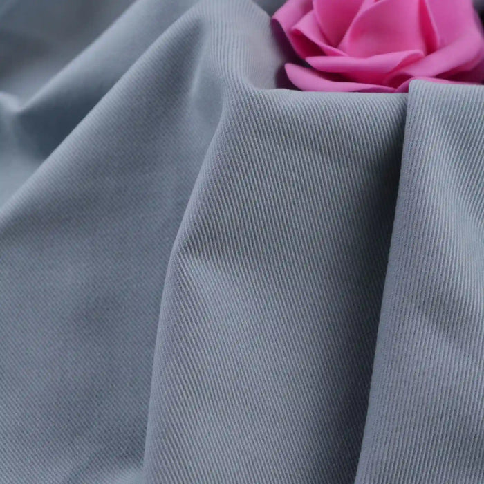 A close-up of Longan Craft’s Multicolor Cotton Bamboo Blend Lyocell Fabric by the yard, shown in light grey with ribbed texture and soft folds, features a pink artificial rose at the top right corner. Ideal for DIY pants and wrinkle-free projects.