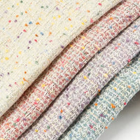 Close-up of four stacked pieces of Longan Craft’s Multicolor Dot Boucle Tweed Fabric By The Yard—a heavyweight jacquard wool blend suiting material in cream, pink, lavender, and light blue hues, each featuring colorful speckled dots throughout the textured weave, evoking the look of classic multicolor bouclé tweed.
