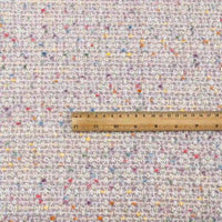 A wooden ruler is placed on the Longan Craft Multicolor Dot Boucle Tweed Fabric By The Yard, a heavyweight jacquard wool blend suiting material. The ruler provides a sense of scale for the fabric’s chic woven texture and colorful specks, highlighting the unique character of this multicolor tweed fabric.