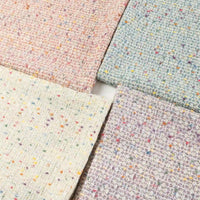 Four swatches of Longan Craft’s Multicolor Dot Bouclé Tweed Fabric By The Yard—a heavyweight jacquard wool blend suiting material—are displayed in pastel pink, blue, cream, and lavender shades. Each features colorful speckles reminiscent of classic multicolor bouclé tweed and are arranged in a square on a white background.