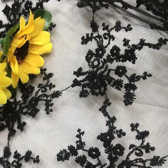The Multicolor Embroidered Floral Tulle Fabric by Longan Craft features colorful cotton thread embroidery on tulle, shown here over a light background with two bright yellow artificial sunflowers on the left.