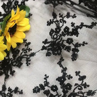 The Multicolor Embroidered Floral Tulle Fabric by Longan Craft features colorful cotton thread embroidery on tulle, shown here over a light background with two bright yellow artificial sunflowers on the left.