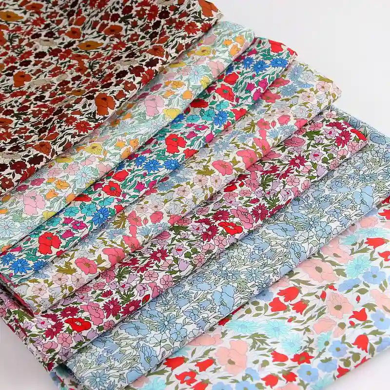 A stack of Longan Craft Multicolor Fine Cotton Printed Lawn Fabric By The Yard, lightweight with assorted floral prints in red, blue, pink, orange, and green—ideal summer material for lawn clothing—neatly arranged on a white surface.