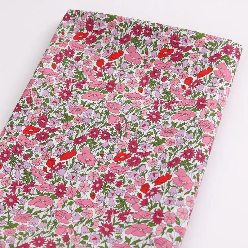 A notebook featuring a cover inspired by Longan Craft's Multicolor Fine Cotton Printed Lawn Fabric, decorated with pink, red, and white floral prints with green leaves on a light background.