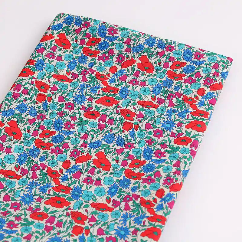 Longan Craft's Multicolor Fine Cotton Printed Lawn Fabric features a vibrant floral print with red, blue, and purple flowers and green leaves on white. Lightweight and ideal for lawn clothing, this material is sold by the yard.