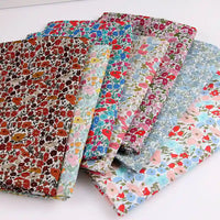 Six pieces of Longan Craft Multicolor Fine Cotton Printed Lawn Fabric are shown overlapping on a white surface. This lightweight floral print material is perfect for summer dresses and lawn clothing.