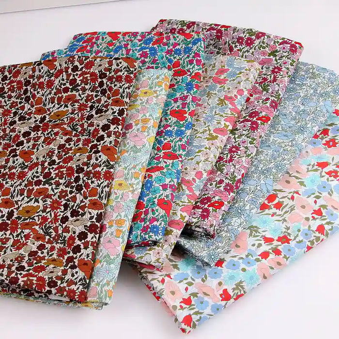 Six pieces of Longan Craft Multicolor Fine Cotton Printed Lawn Fabric are shown overlapping on a white surface. This lightweight floral print material is perfect for summer dresses and lawn clothing.