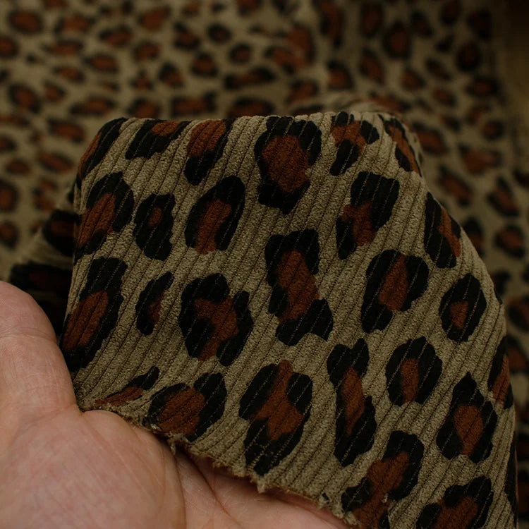 A hand displays Longan Craft's Multicolor Leopard Printed Corduroy Fabric By The Yard, a bold animal printed polyester corduroy textile, with its vibrant pattern shown against matching soft corduroy material.