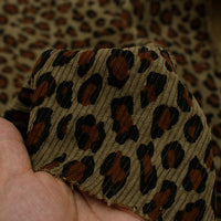 A hand displays Longan Craft's Multicolor Leopard Printed Corduroy Fabric By The Yard, a bold animal printed polyester corduroy textile, with its vibrant pattern shown against matching soft corduroy material.