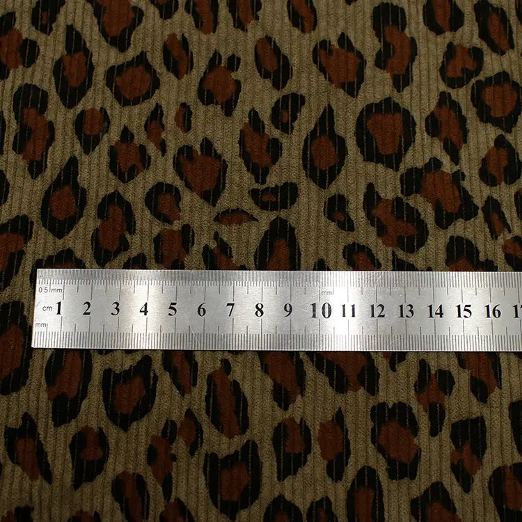 A metal ruler shows centimeter and millimeter scale on Longan Craft's Multicolor Leopard Printed Corduroy Fabric by the Yard, a soft animal print polyester corduroy textile featuring brown, black, and tan patterns for apparel.