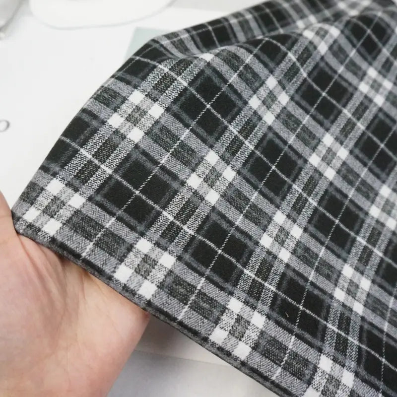 A hand holds a piece of Longan Craft Multicolor Mammoth Flannel Fabric by the yard, showcasing its cozy brushed texture and plaid pattern—ideal for pants and crafted from high-quality flannel textile.