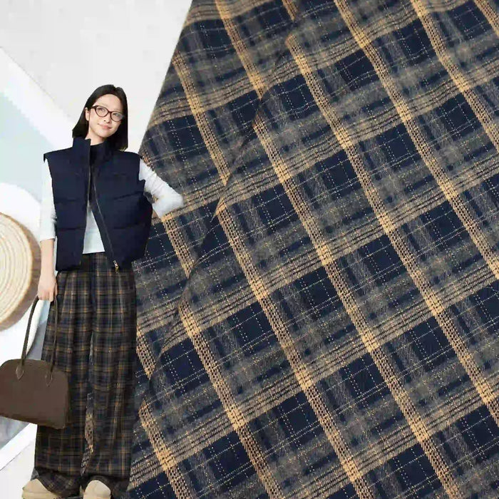 A woman wearing glasses, a navy vest, and wide-leg plaid pants holds a brown bag. The background displays Longan Craft Multicolor Mammoth Plaid Brushed Flannel Fabric, perfect for cozy pants.