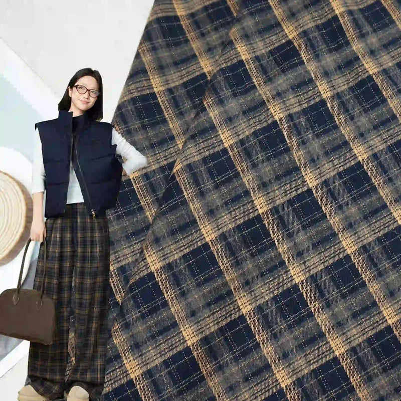 A woman wearing glasses, a navy vest, and wide-leg plaid pants holds a brown bag. The background displays Longan Craft Multicolor Mammoth Plaid Brushed Flannel Fabric, perfect for cozy pants.