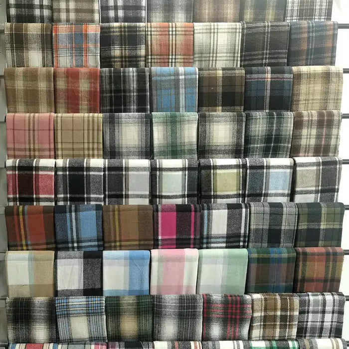 Longan Craft's Multicolor Plaid Mammoth Flannel Fabric by the yard, a brushed polyester cotton textile ideal for shirts, is neatly arranged on display shelves and features a variety of vibrant checkered designs.