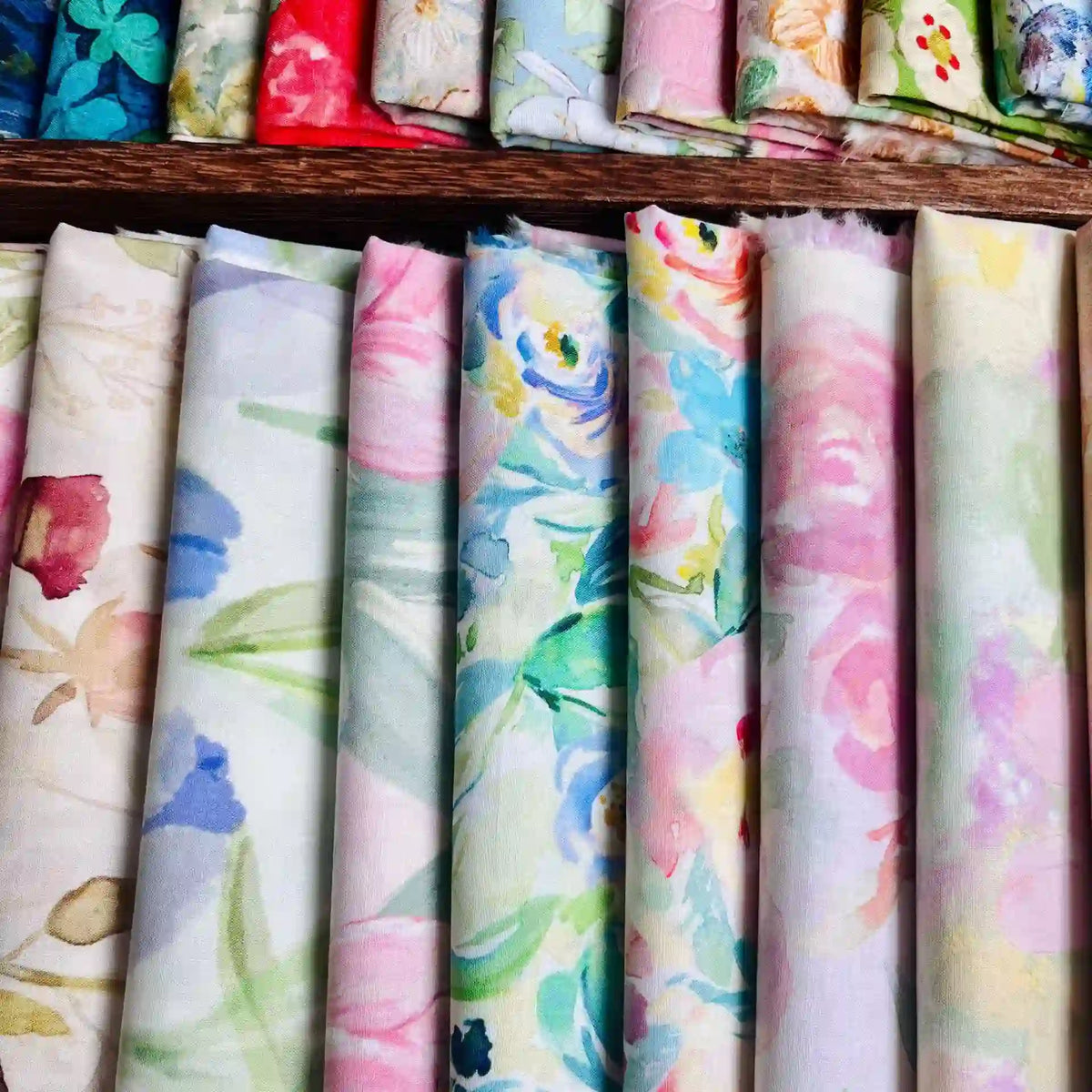 Longan Craft's Multicolor Printed Lawn Fabric By The Yard features soft pastel florals in pink, blue, green, yellow, and white on cotton lawn material, neatly arranged on a wooden surface.