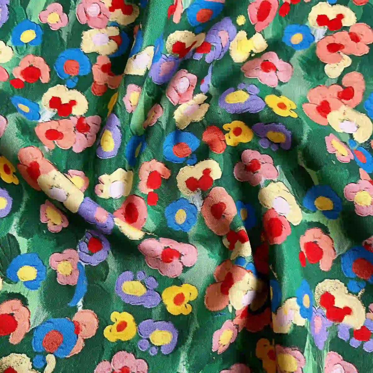 A close-up of Longan Craft’s Multicolor Printed Lawn Fabric by the yard—a soft cotton lawn cloth with a vibrant floral print in red, yellow, pink, and blue. The slightly crumpled fabric forms gentle folds and textured shadows.