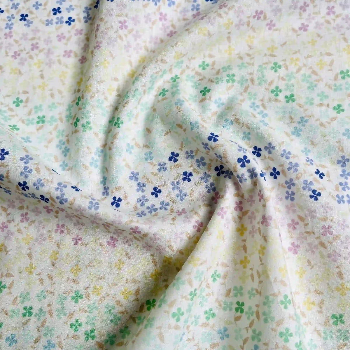 A close-up of Longan Craft’s Multicolor Printed Floral Cotton Lawn Fabric by the yard, showing its soft, textured cotton material with a pastel gradient and scattered multicolored four-petal flowers.
