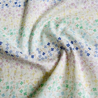 A close-up of Longan Craft’s Multicolor Printed Floral Cotton Lawn Fabric by the yard, showing its soft, textured cotton material with a pastel gradient and scattered multicolored four-petal flowers.
